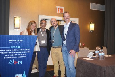 Four individuals stand together and smile beside a conference sign.