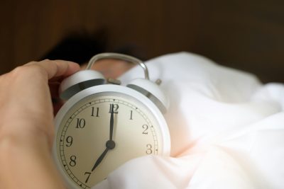 Hand holding clock in bed sheets.